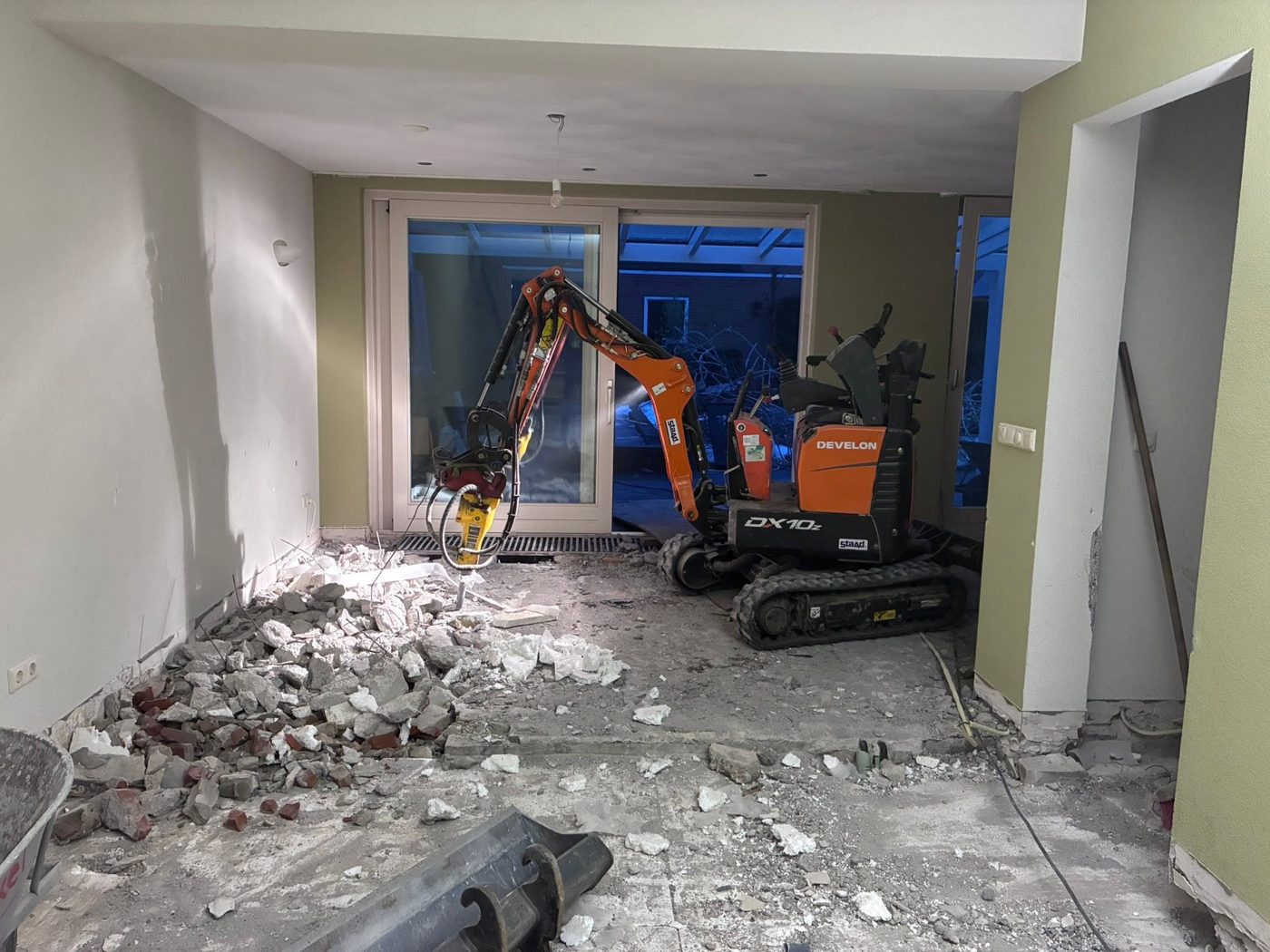 Minigraver met hakhamer bij het sloopwerk van een betonvloer in een woning